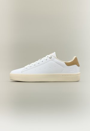 Scarpa da ginnastica bianca a taglio basso con suola beige e toppa in pelle scamosciata color cuoio sul tallone, design con lacci e dettagli minimi di perforazione sul lato.