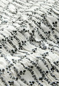 Tissu blanc à motif floral noir, avec des sections élastiques froncées et des boutons recouverts de tissu.