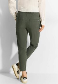 Groene katoenen broek met een taps toelopende pasvorm, voorzien van een rekbare tailleband, twee achterzakken en subtiele stikseldetails. Gedragen met witte sneakers.