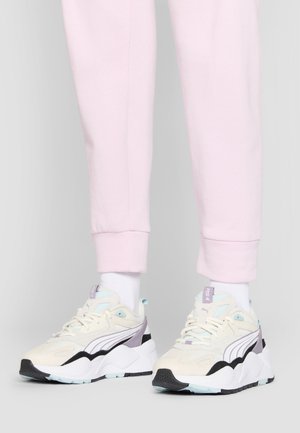 Sport shoes in cream, light blue, and black. Suede and mesh materials with thick white sole and purple accents. Worn with pink joggers.