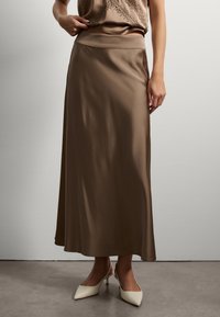 Jupe maxi en satin marron avec une texture lisse et une taille élastique, associée à des talons slingback crème avec un design à bout pointu.