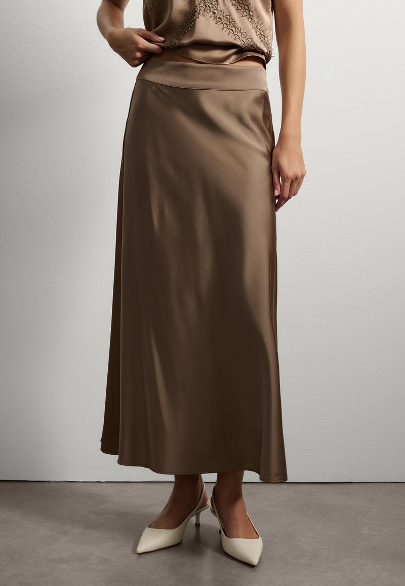 Jupe maxi en satin marron avec une texture lisse et une taille élastique, associée à des talons slingback crème avec un design à bout pointu.