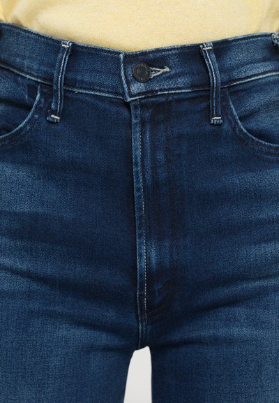 Jeans de mezclilla de tiro alto en azul oscuro con un clásico diseño de cinco bolsillos, que cuentan con un botón de latón y costuras en contraste.