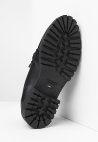 Semelle de botte en cuir noir avec motif de traction profond, présentant une surface lisse et plate ainsi qu'une étiquette rectangulaire en relief sur le côté.
