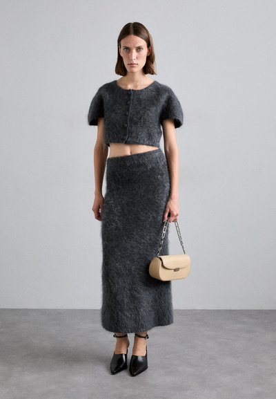 Grijze mohair crop top met korte mouwen en knopen, gecombineerd met een grijze, gestructureerde lange rok. Accessoires omvatten een beige handtas en zwarte puntige schoenen.