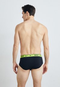 Schwarze Nike-Unterwäsche mit einem leuchtend grünen elastischen Bund, glatter Textur, mittelhohem Schnitt und ohne sichtbare Muster auf dem Stoff.