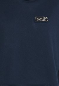 Sudadera azul marino hecha de un tejido suave, con un pequeño logo bordado en negro de Levi's en la parte superior izquierda. Textura suave.