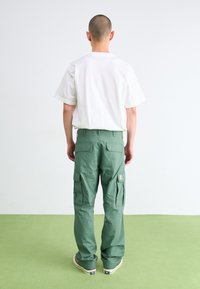 Chemise blanche à manches courtes associée à un pantalon cargo vert avec poches et écusson. Texture lisse avec une coupe décontractée.