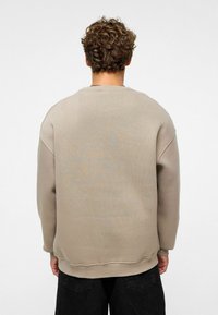 Beige sweatshirt met een losse pasvorm, ribgebreide boorden en zoom. Gladde textuur met minimale stikdetails. Draagt over donkere broeken.