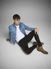 Chaqueta de denim en azul claro, usada sobre una camiseta blanca. Jeans negros de corte ajustado con textura suave. Botines de ante marrón.