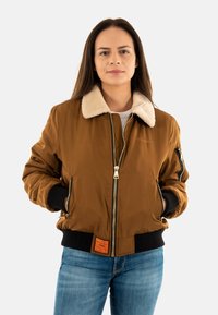 Giacca bomber marrone con colletto in pelliccia sintetica, polsini e orlo a coste. Presenta tasche con zip e un'etichetta del marchio sul davanti.