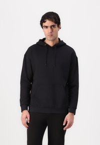 Hoodie noir en pullover en tissu à texture lisse, avec une poche avant, des cordons ajustables et des poignets côtelés.