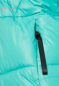 Tissu matelassé bleu sarcelle avec une sangle noire ajustable enroulée à travers une petite ouverture, faisant partie d'un vêtement d'extérieur ou d'hiver.