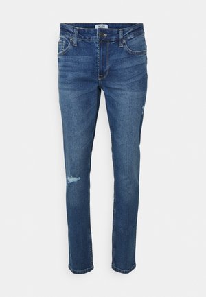 Jeans de ganga azul-escuro com um corte justo, apresentando desbotamento ligeiro na coxa esquerda, cinco bolsos e uma cintura costurada.