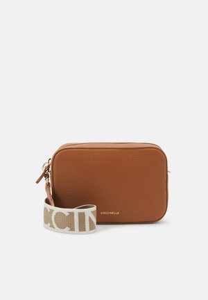 Rectangular brown leather crossbody bag with a white fabric strap featuring large beige lettering, gold zipper, and small gold brand logo.