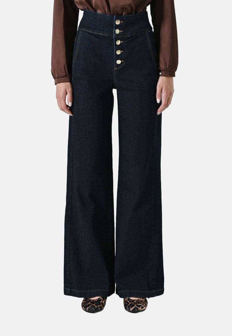 Jean en denim foncé taille haute avec un devant à cinq boutons, une coupe large, des accents en métal doré et des détails de couture contrastés.