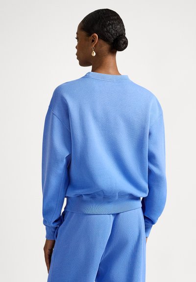 Sweatshirt azul feita de tecido macio, com gola redonda, punhos canelados e um corte descontraído. A parte de trás tem uma textura suave e costuras.