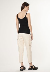 Top nero senza maniche con bordino in pizzo, abbinato a pantaloni cargo beige chiaro con tasche laterali e sandali neri chunky. Sfondo neutro.