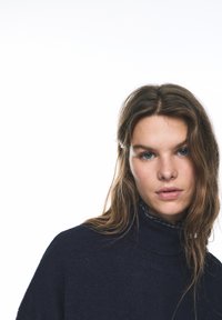 Granatowy sweter z golfem z prążkowanym kołnierzem, miękką teksturą i dopasowanym krojem, noszony na koszuli z kołnierzykiem w kratę.