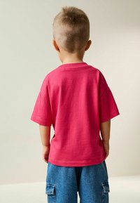 Lyserød bomulds t-shirt med korte ærmer og rund hals, båret med blå denim cargo-shorts, set bagfra.