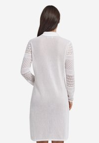 Biała dzianinowa sukienka z kołnierzykiem, z ażurowymi koronkowymi wstawkami na rękawach. Materiał jest lekki i półprzezroczysty.
