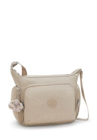 Beige shoulder bag made of textured fabric, featuring a front zipper pocket, logo detail, and a plush monkey charm attached.