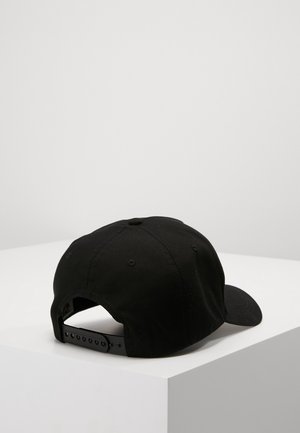 Czarna regulowana czapka typu snapback umieszczona na białym stole ekspozycyjnym, widziana od tyłu z zakrzywionym daszkiem skierowanym w prawo.