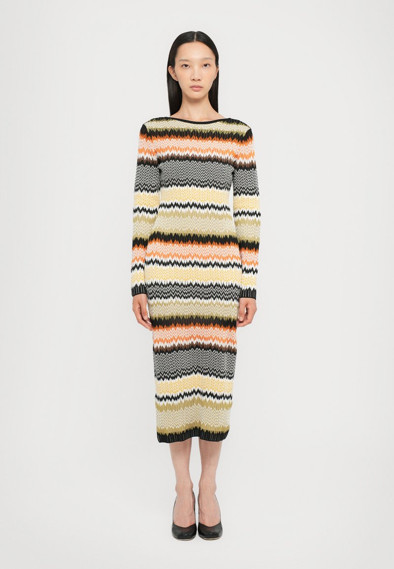 Abito lavorato a maglia con strisce zigzag multicolori in arancione, nero, giallo e crema. Maniche lunghe, forma aderente e lunghezza fino al polpaccio.