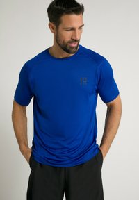 Blå atletisk T-shirt lavet af glat stof, med korte ærmer og et subtilt logo i guld på venstre brystområde.