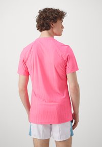 Fitted short-sleeve t-shirt in bright pink, featuring a textured pattern and a crew neckline. Back view shows raglan sleeves and smooth finish.