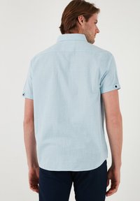 Camisa de botones de manga corta de color azul claro, con un tejido texturizado, cuello y detalles de puños enrollados. Parte trasera lisa con un dobladillo recto.