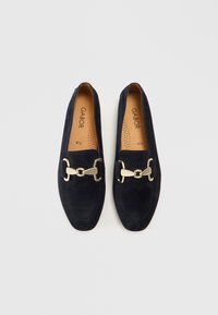 Navy suede loafers with a flat sole, featuring a gold-tone chain accent on the vamp. Interior has perforated detailing for breathability.