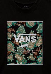 Camiseta negra con un gráfico floral en verde y beige, con "VANS" destacado en texto blanco en negrita y un icono de patineta.