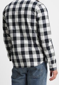 Camicia a maniche lunghe con bottoni, caratterizzata da un motivo a scacchi bianco e nero, realizzata in tessuto tessuto con una finitura testurizzata.