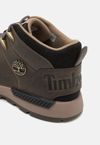 Zapato de senderismo de piel marrón con un collar acolchado, acento texturizado cerca de la suela, logo grabado y panel de ante oscuro en contraste.