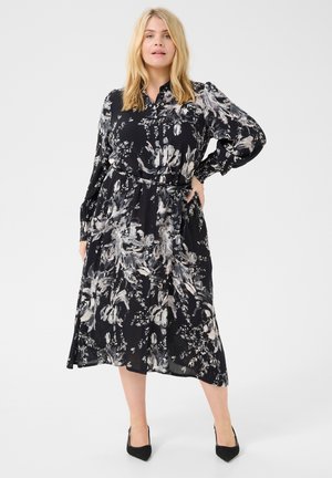 Vestido negro con flores, de mangas largas, con botones en la parte delantera y lazo en la cintura. Presenta un diseño fluido con patrones florales de colores claros.