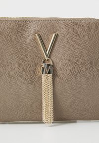 Brown textured leather pouch with a gold-tone metal V-shaped zipper pull, featuring a decorative chain tassel and a metal accent.