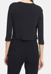 Black cropped top with three-quarter sleeves, smooth texture, rounded neckline, and a slightly curved hem, paired with black high-waisted trousers.