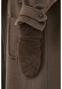 Rudos vilnos paltos rankovė su sagomis ant dirželio virš minkštos, purios rudos kumštinės pirštinės, dengiančios ranką.