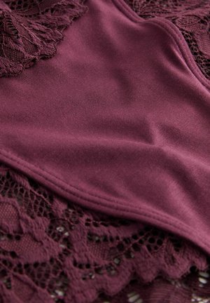 Close-up of burgundy fabric with smooth, solid section overlaying intricate floral lace pattern.