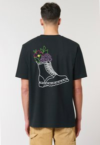 Zwarte T-shirt met geborduurd ontwerp van een laars met bloemen in levendige kleuren op de achterkant. Korte mouwen en een relaxte pasvorm.
