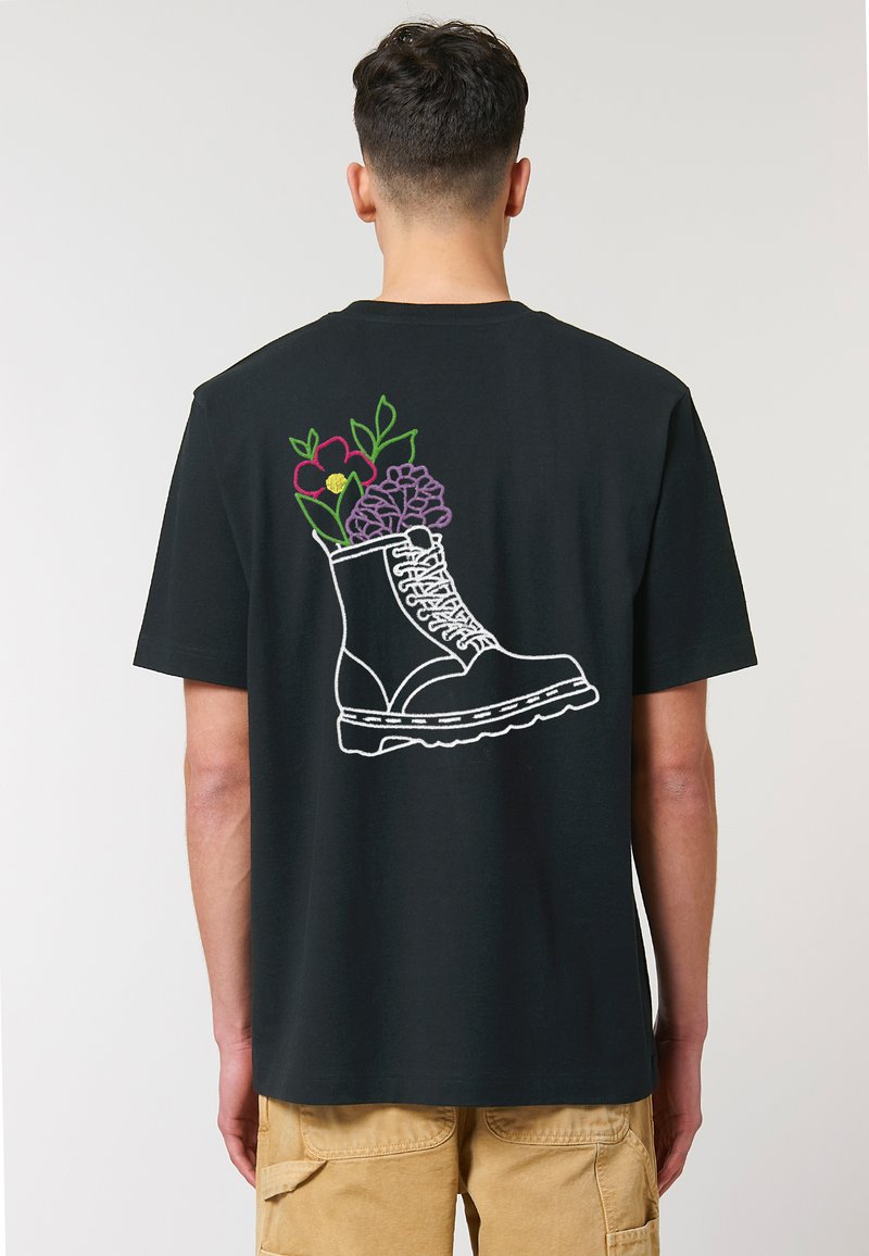 Zwarte T-shirt met geborduurd ontwerp van een laars met bloemen in levendige kleuren op de achterkant. Korte mouwen en een relaxte pasvorm.