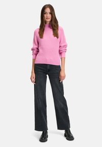Roze geribde trui met een hoge hals, gecombineerd met wijde donkere spijkerbroek en zwarte enkellaarsjes. De outfit heeft een textuur in het breisel.