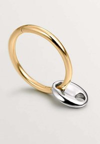 Anillo circular color dorado con un acabado suave, que presenta un acento ovalado plateado con un pequeño agujero. Diseño minimalista.