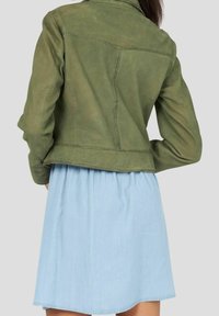 Olivengrøn læderjakke med en tætsiddende design, der har synlige sømdetaljer. Kombineret med en lyseblå, flagrende denimnederdel.
