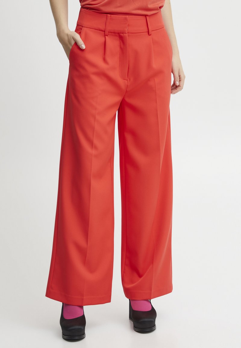 Red wide-leg trousers with a smooth texture, featuring front pleats and side pockets. Paired with black shoes and pink socks.