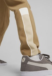 Joggers beige con pannello laterale bianco e dettagli in piping, abbinati a sneakers grigie in suede con logo bianco e suola testurizzata.