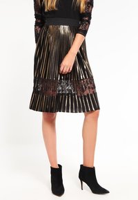 Fållad svart och guldram kjol med metalliska ränder, en spetsdetalj och ett svart elastiskt midjeband. Matchad med svarta ankelstövlar.