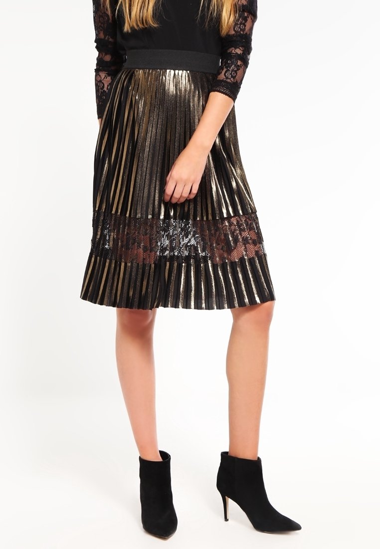 Fållad svart och guldram kjol med metalliska ränder, en spetsdetalj och ett svart elastiskt midjeband. Matchad med svarta ankelstövlar.