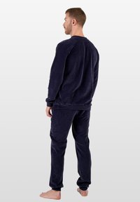 Granatowy prążkowany komplet do domu składający się z długiego rękawa i spodni z elastycznym pasem. Tkanina ma miękką teksturę i luźny krój.
